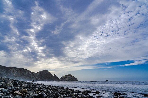 Ein Strand bedeckt mit schwarzen Felsen unter strahlenden Wolken