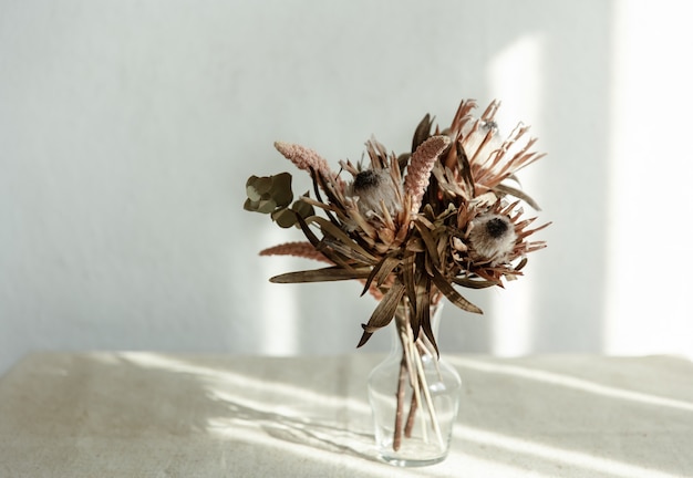 Ein Strauß getrockneter Blumen in einer Glasvase auf hellem Hintergrund mit Sonnenlicht.