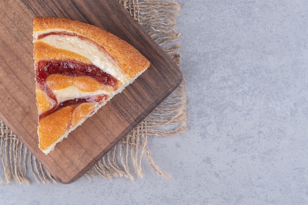 Ein Stück Kuchen auf einem Holzbrett auf Marmortisch.