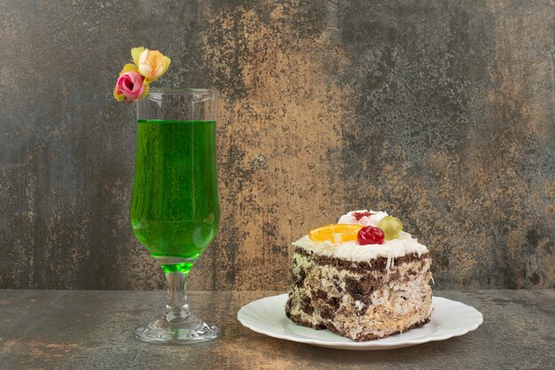 Ein Stück Kuchen mit einem Glas saftiger grüner Limonade auf Marmorwand