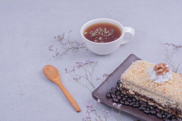 Ein Stück Medovic-Kuchen mit Schokoladenbohnen auf einer schwarzen Platte mit einer Tasse Tee