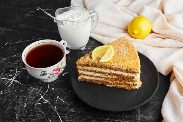 Ein Stück Medovic-Kuchen mit Zitrone, Quark und einer Tasse Tee.