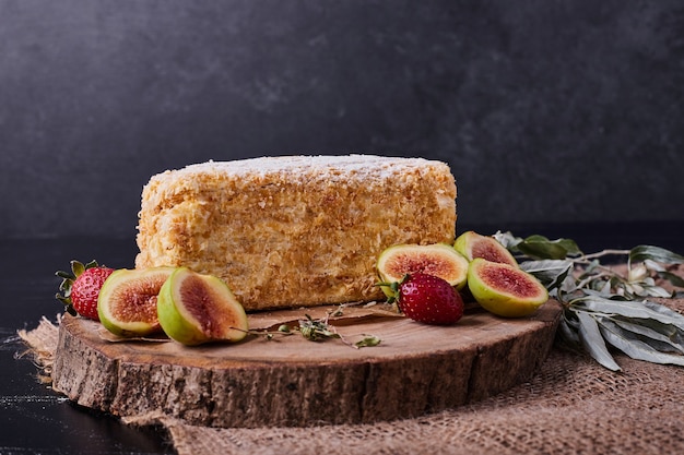 Ein Stück Napoelon-Kuchen auf dunklem Hintergrund mit Feigen und Erdbeeren.