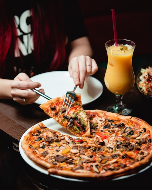 Kostenloses Foto ein stück pizza mit gemischten zutaten mit einem glas orangensaft einnehmen.