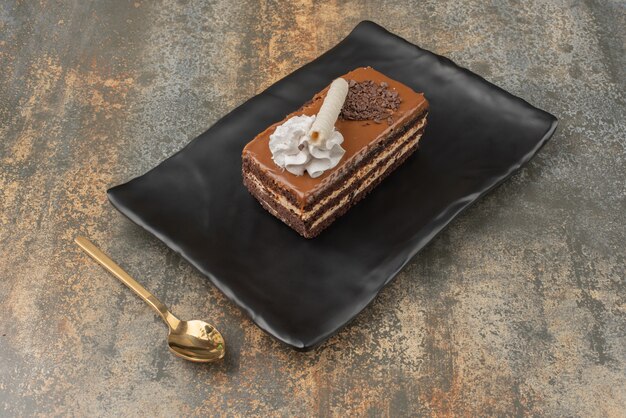 Ein Stück süßer Kuchen mit goldenem Löffel auf dunklem Teller