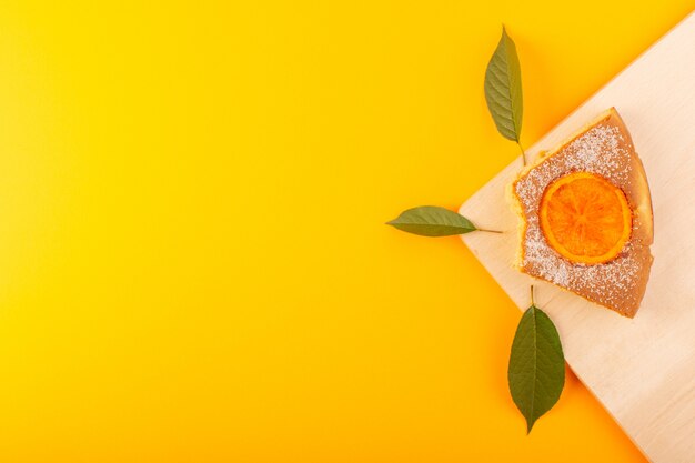 Ein süßer köstlicher leckerer Orangenkuchen des Draufsichts auf dem cremefarbenen Holzschreibtisch und dem süßen Zuckerkeks des gelben Hintergrunds