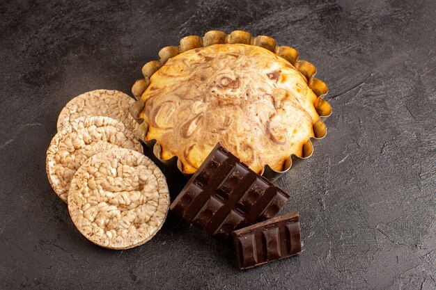 Ein süßer runder Kuchen der Draufsicht leckeres leckeres inneres Kuchenpfannen zusammen mit Schokoriegeln und Brotchips auf dem grauen Hintergrundkekszuckerplätzchen