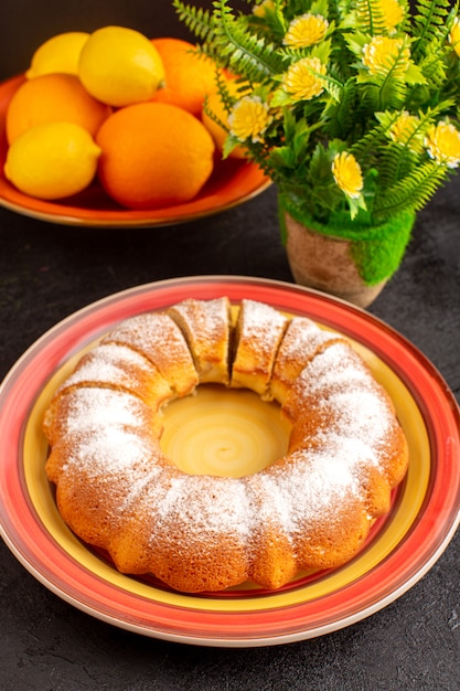 Ein süßer runder Kuchen der Draufsicht mit Zuckerpulver geschnitten süßer köstlicher isolierter Kuchen innerhalb Platte zusammen mit Zitronen und grauem Hintergrundkekszuckerplätzchen