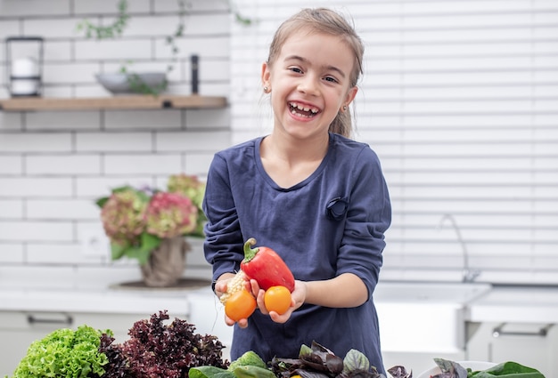 Kostenloses Foto ein süßes kleines mädchen hält frisches gemüse, während es einen salatkopierraum vorbereitet.