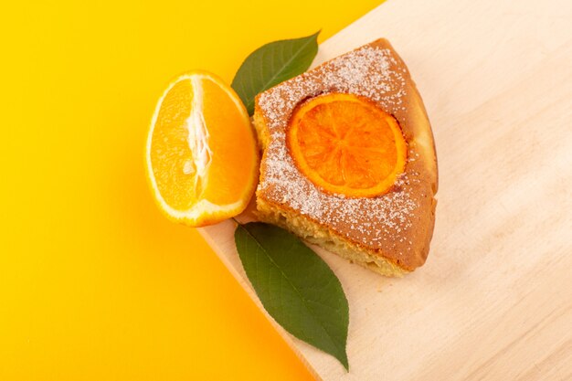 Ein süßes leckeres leckeres Stück des Orangenkuchenstücks der Draufsicht auf dem cremefarbenen Holzschreibtisch und dem süßen Zuckerkeks des gelben Hintergrunds