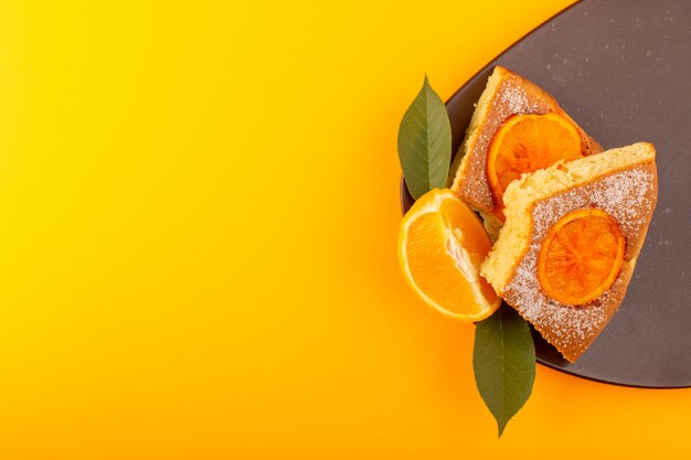 Ein süßes leckeres leckeres Stück Orangenkuchenscheibe von oben, auf dem braunen Holzschreibtisch und dem süßen Zuckerkeks des gelben Hintergrunds