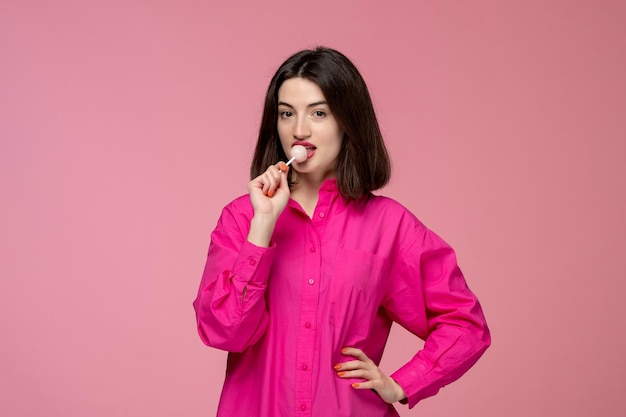 Ein süßes Mädchen, ein hübsches, junges, wunderschönes, brünettes Mädchen in einem rosa Hemd, das einen Lippenstift leckt.