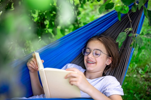 Ein süßes Mädchen liest ein Buch in einer Hängematte im Garten