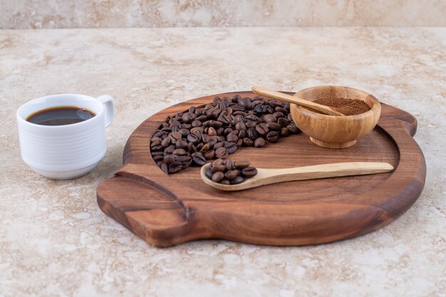 Ein Tablett mit gemahlenen und ganzen Kaffeebohnen neben einer Tasse Kaffee