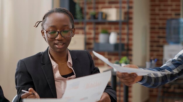 Ein Team afroamerikanischer Kollegen analysiert Verkaufsberichte zu Dokumenten und arbeitet an einer Finanzstrategie für das Unternehmenswachstum. Mitarbeiter des Unternehmens, die Teamarbeit mit Diagrammpapieren leisten. Handschuss.