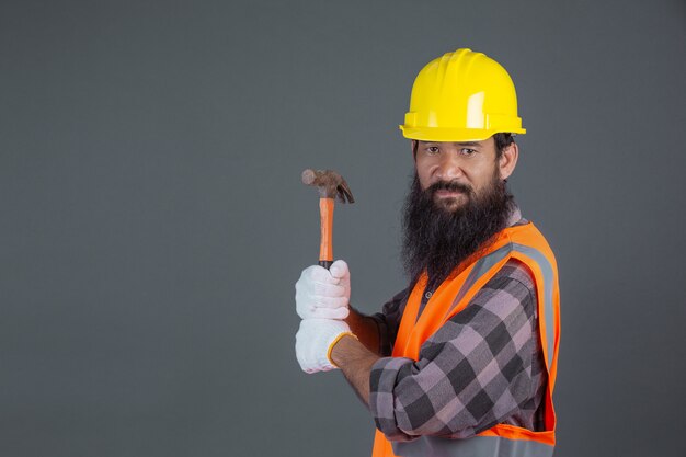 Ein Technikmann, der einen gelben Sturzhelm mit Baugeräten auf einem Grau trägt.