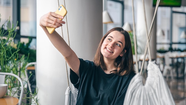 Kostenloses Foto ein teenager-mädchen sitzt in einer aufgehängten hängematte und macht ein selfie auf einem smartphone