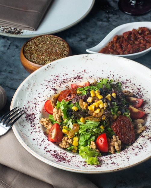 Ein Teller mit grünem Salat mit Salat, Tomaten, Walnuss, Mais und Rosinen