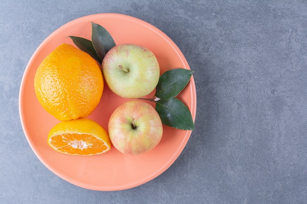 Ein Teller mit leckerem Apfel und Orangen auf Marmortisch.