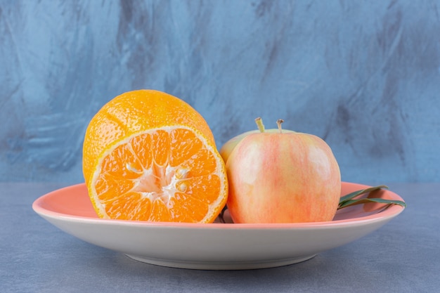 Ein Teller mit leckeren Äpfeln und Orangen auf der dunklen Oberfläche