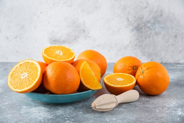 Ein Teller voller geschnittener und ganzer saftiger Orangenfrüchte mit Holzreibahle.