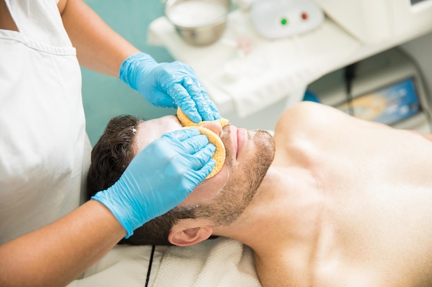 Ein Therapeut führt bei einem jungen Mann während seines Besuchs in einem Spa eine Gesichtsreinigung durch