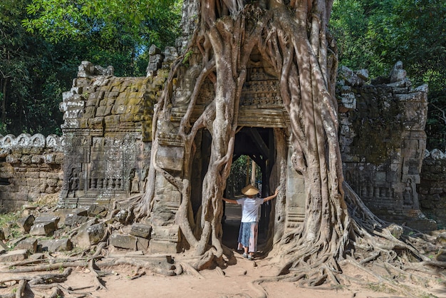 Ein tourist, der angkor-ruinen unter dschungel, angkor wat tempelkomplex, reiseziel kambodscha besucht. frau mit traditionellem hut, hintere ansicht.