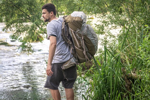 Ein Tourist mit einem großen Wanderrucksack in der Nähe eines Gebirgsflusses in der Sommerhitze.