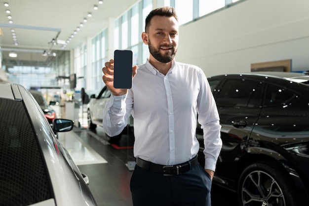 Ein verkäufer in einem autohaus demonstriert den bildschirm eines smartphones vor dem hintergrund von neu Premium Fotos