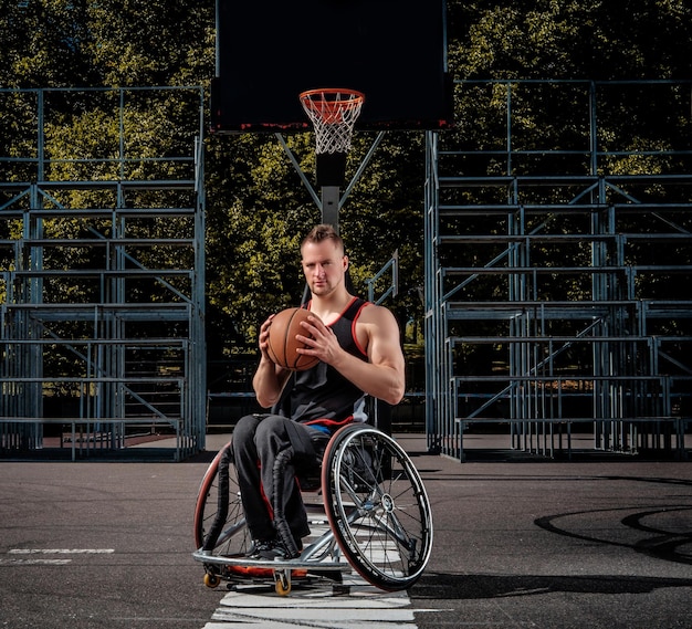 Ein verkrüppelter Basketballspieler im Rollstuhl hält einen Ball auf einem offenen Spielfeld.