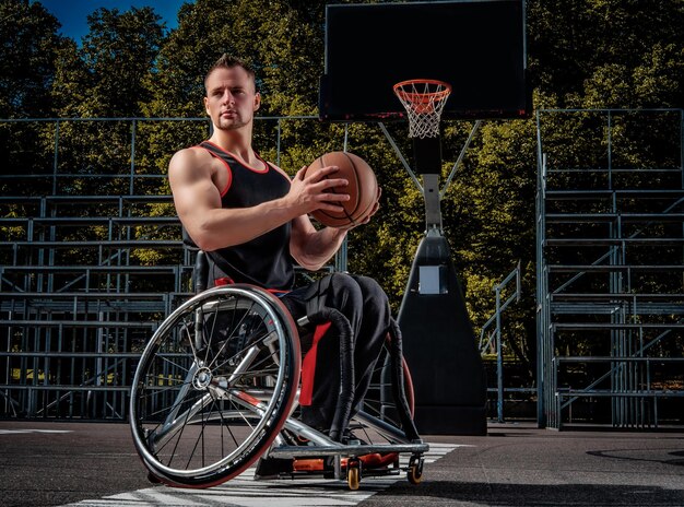 Ein verkrüppelter Basketballspieler im Rollstuhl hält einen Ball auf einem offenen Spielfeld.