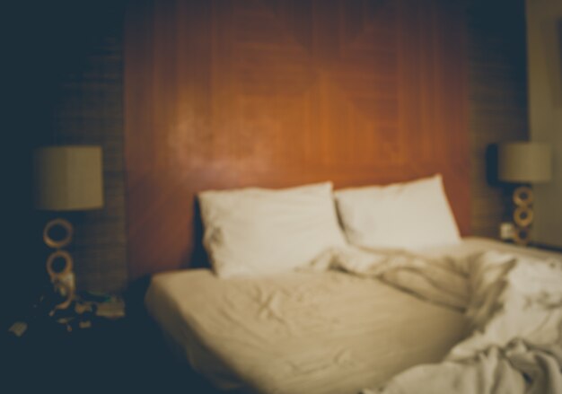 Ein verschwommenes unordentliches Bett mit weißer Bettwäsche im Vintage-Ton.