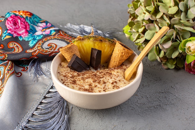 Ein vorderes geschlossenes Ansichtschoko-Dessertbraun mit Ananasscheiben-Schokoriegel-Eiscreme innerhalb des weißen Tellers zusammen mit Taschentuch und Blumen auf dem Grau