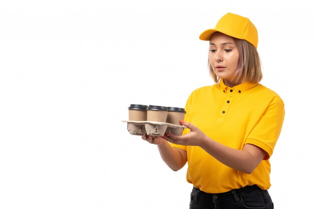 Ein weiblicher Kurier der frotn Ansicht im gelben Hemd der gelben Kappe und in den schwarzen Jeans, die Tassen Kaffee halten