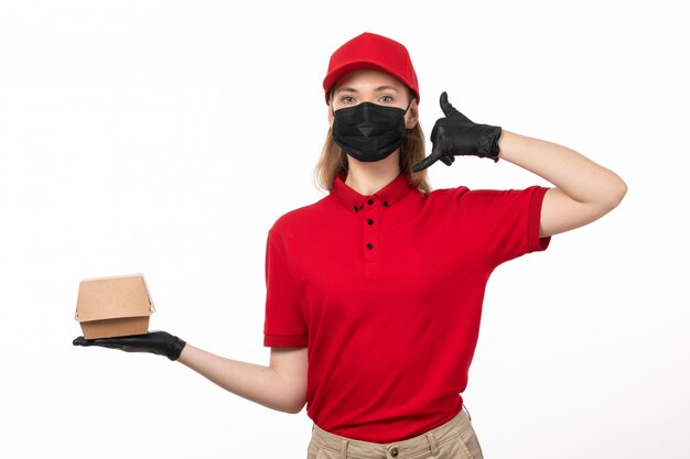 Ein weiblicher Kurier der Vorderansicht in den roten Handschuhen der roten Kappe der roten Kappe und der schwarzen Maske, die Lebensmittelpaket hält