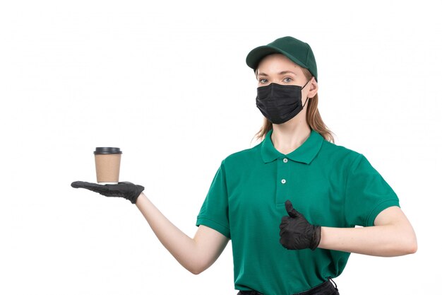 Ein weiblicher Kurier der Vorderansicht in den schwarzen Handschuhen der grünen Uniform und der schwarzen Maske, die Kaffeetasse hält