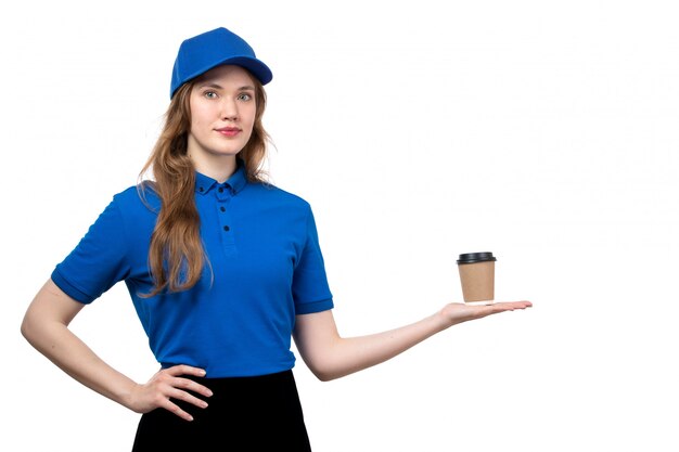 Ein weiblicher Kurier der Vorderansicht in der blauen Kappe des blauen Hemdes und in der schwarzen Hose, die Kaffeetasse auf Weiß hält