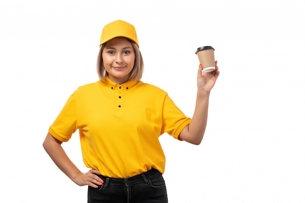Ein weiblicher Kurier der Vorderansicht in der gelben Kappe der schwarzen Jeans der gelben Kappe, die Kaffee auf Weiß hält