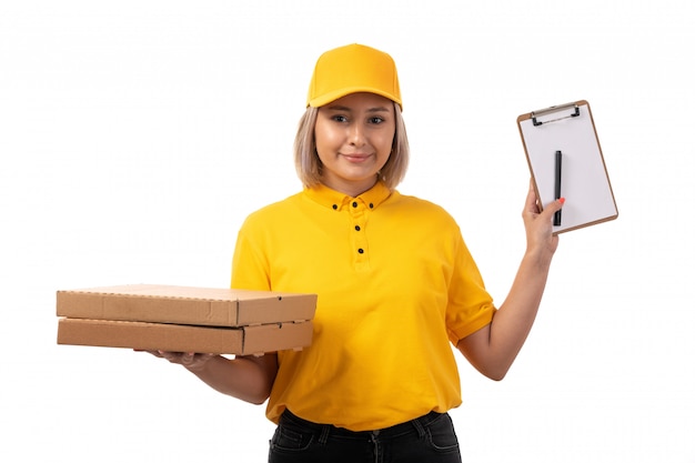 Ein weiblicher Kurier der Vorderansicht in der gelben Kappe der schwarzen Jeans des gelben Hemdes, die Pizzakartons auf weiß lächelnd hält
