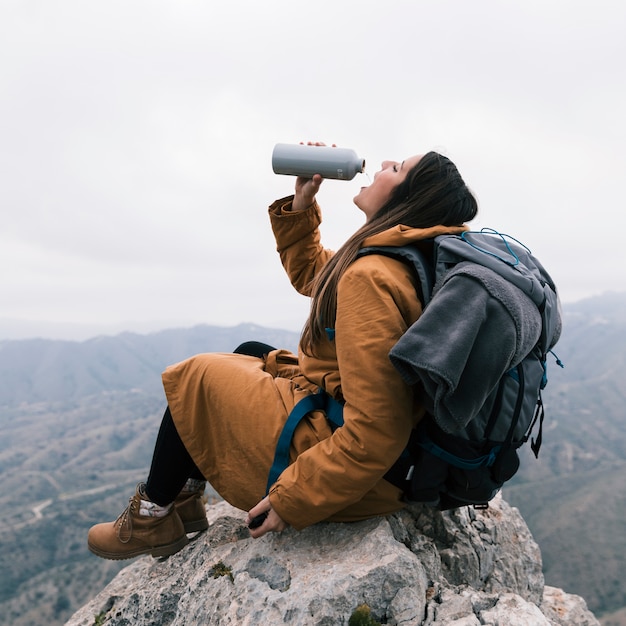 Ein weiblicher Wanderer, der auf den Berg das Wasser von der Flasche trinkend sitzt
