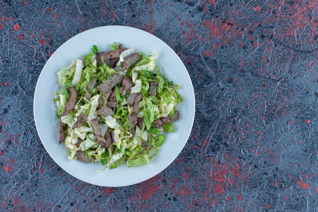 Ein weißer Fleischteller mit Gemüsesalat.