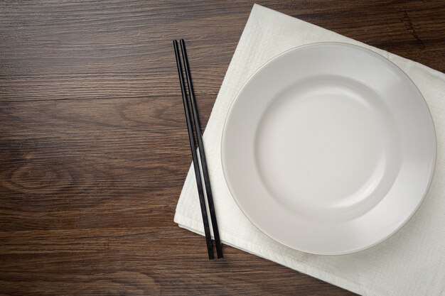 Ein weißer runder leerer Teller und Essstäbchen auf Holztisch