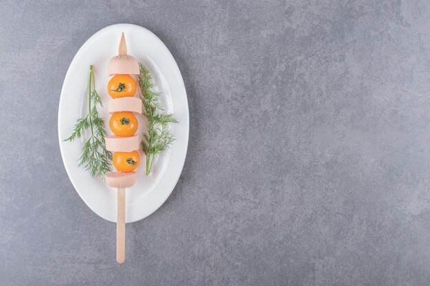 Ein weißer Teller mit gekochter Wurstscheibe mit kirschgelber Tomate.