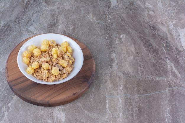 Ein weißer Teller mit gesunden Cornflakes auf einem runden Holzbrett.