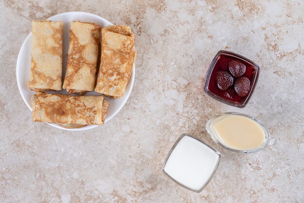 Ein weißer Teller mit leckeren Crepes und Erdbeermarmelade