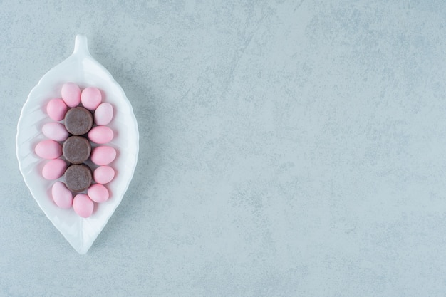 Ein weißer Teller mit süßen rosa Bonbons und Schokoladenkeksen auf weißer Oberfläche