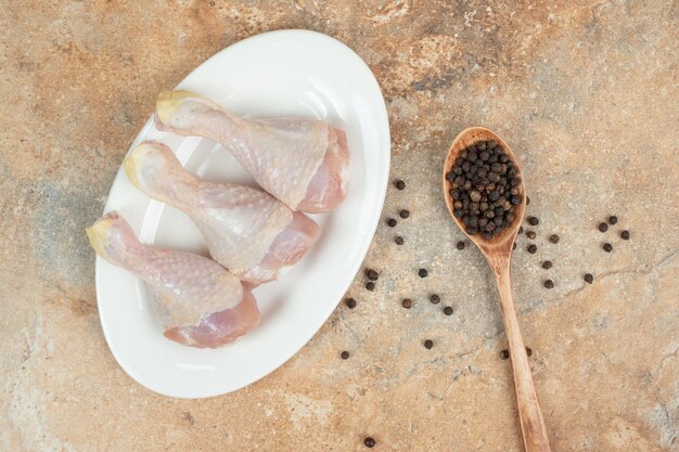 Ein weißer Teller mit ungekochtem Hähnchenschenkel mit Holzlöffel Pfeffer