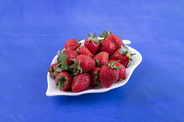 Ein weißer Teller voller Erdbeeren auf blauer Oberfläche