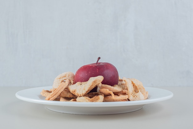 Ein weißer Teller voller getrockneter Apfelfrüchte mit einem ganzen Apfel.