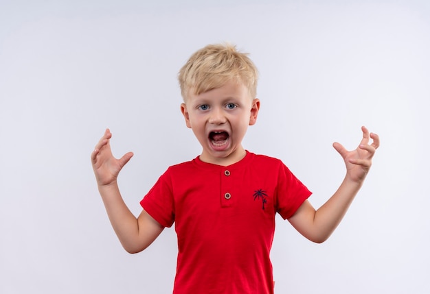 Ein wütender kleiner süßer blonder Junge im roten T-Shirt, der mit seinen Händen schreit